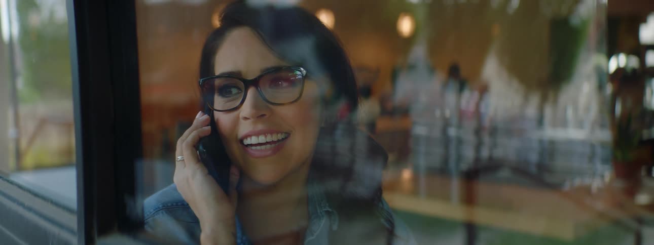 A woman sitting in a cafe looks out of the windows as she speaks on her smartphone