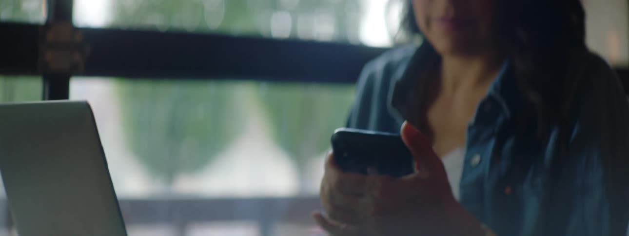 Young woman wearing glasses working on a laptop takes a call on her smartphone