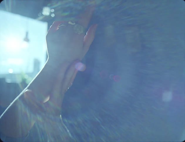 Sunlight flares through a room window where a woman rubs her hands on the air