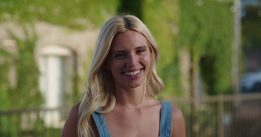 A blonde haired woman laughs while standing next to an ivy covered building