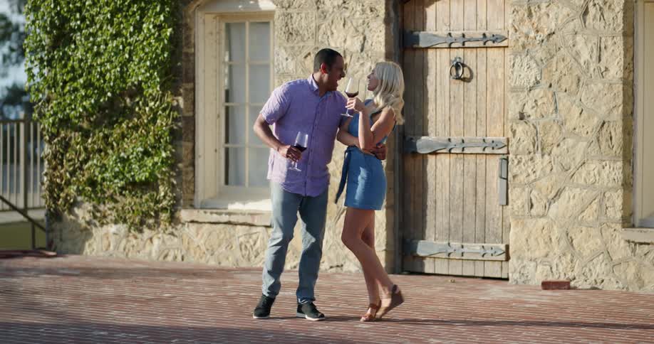 A man and woman dance outside while drinking wine