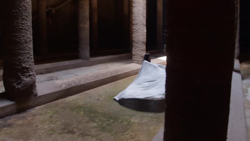 A woman in a costume spinning and dancing in a room with pillars
