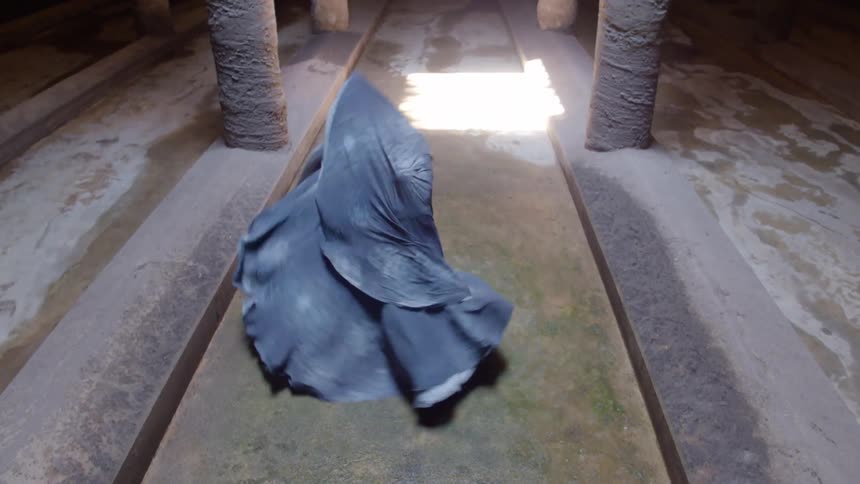 A woman with material flowing off of her spins as she dances in a building with large columns