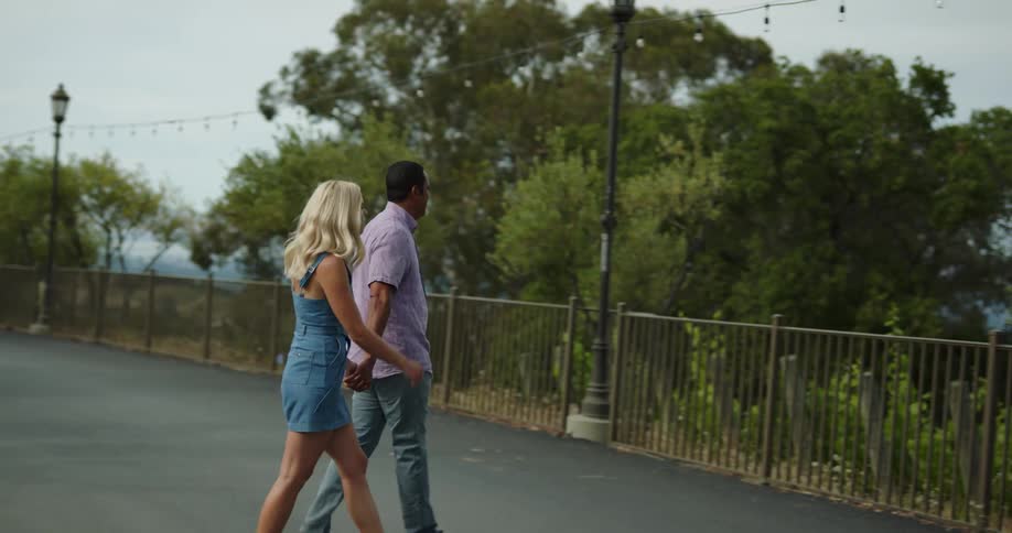 A man and woman walk down a driveway and across a rural road to a fence and look at the scenery