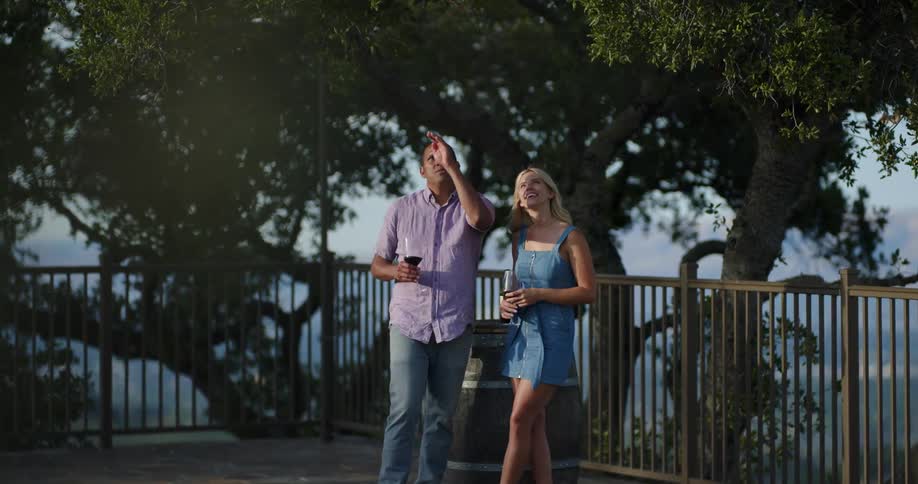 A man and woman stand on a large balcony holding wine glasses