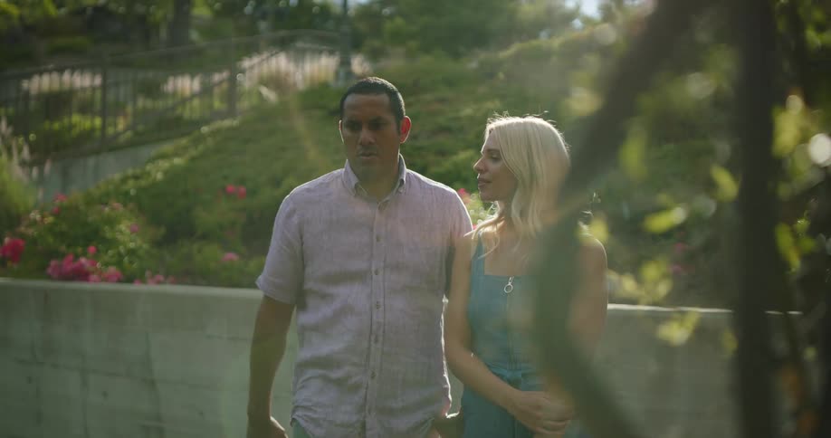 A man gestures and speaks to a young woman before leading her out of frame
