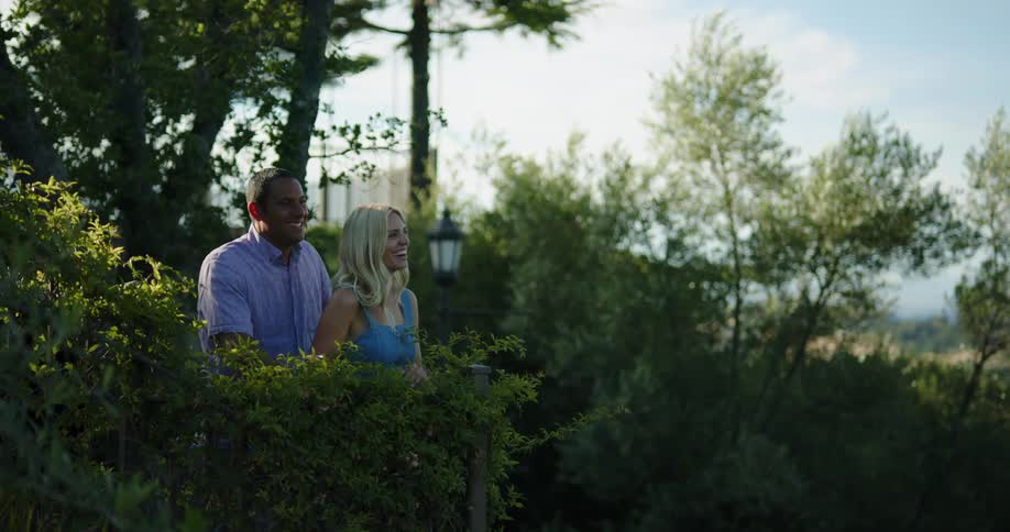 A man puts his arms around his girlfriends waist as they look up at the trees in a park