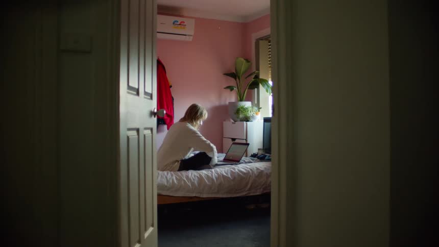 A teenage girl sitting on her bed in her room looks at her laptop