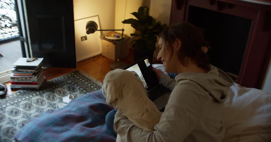 A woman sits on the couch with her dog having a video call on a tablet