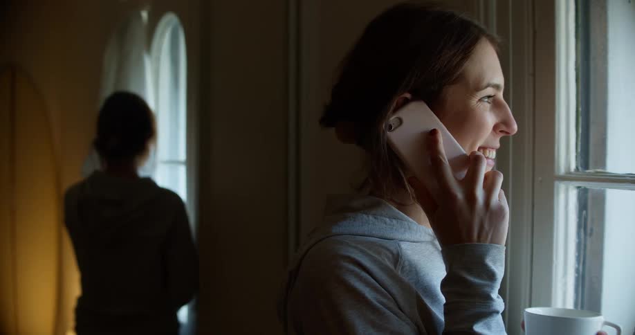 A woman talks on her cell phone with a drink by the window