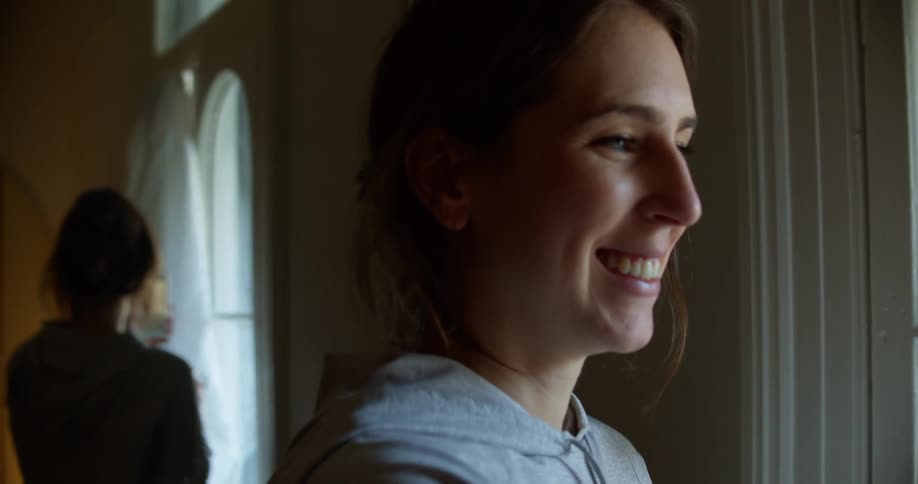 A woman holds a cell phone up having a video call while standing next to a window with a coffee mug