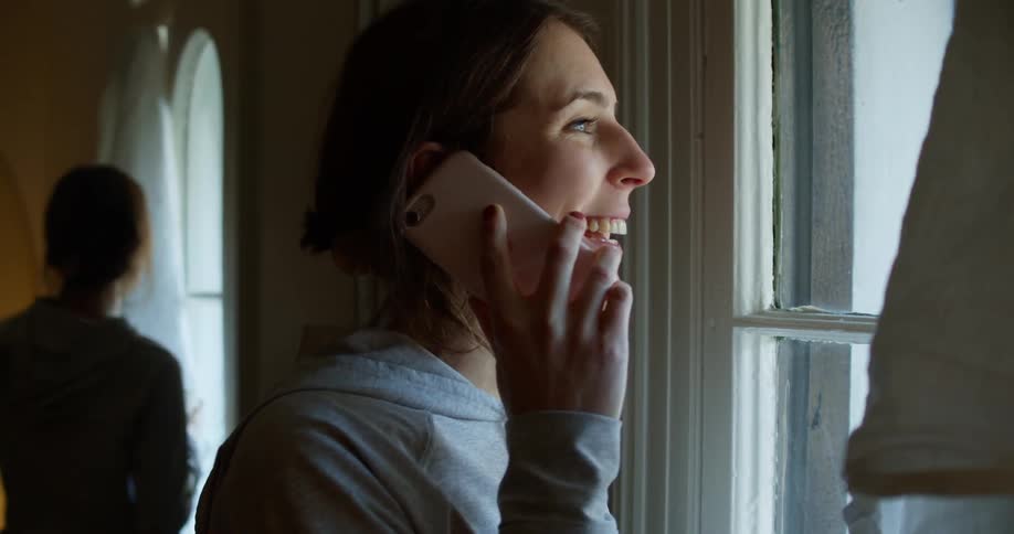 Mirror reflects woman standing near window talking on mobile phone and holding coffee mug