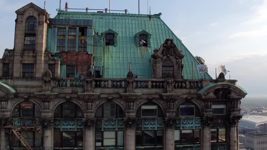 A large gothic style apartment building with an atrium rooftop sits in the center of a modern downtown city