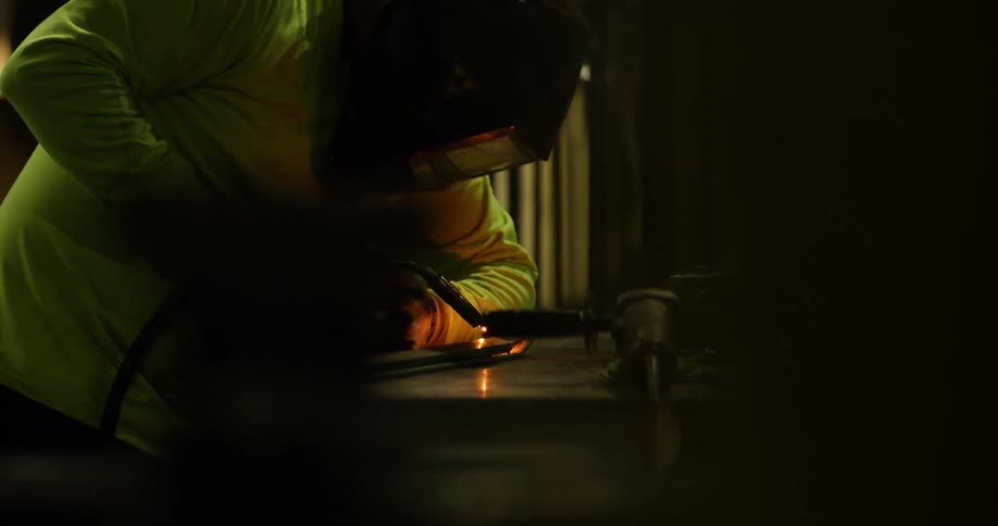 A person with a torch and a welding helmet welding with lights and sparks