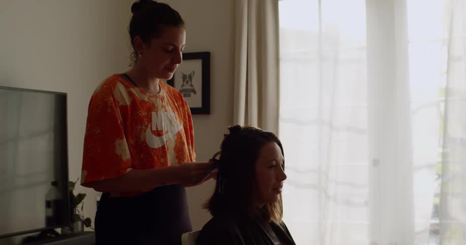 A woman stands behind another woman placing hair color foils in her hair