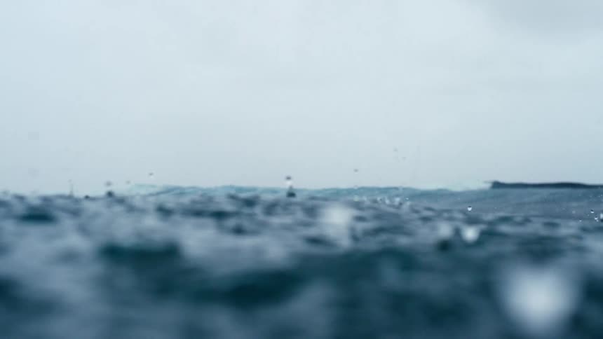 Rain drops fall into rough ocean water