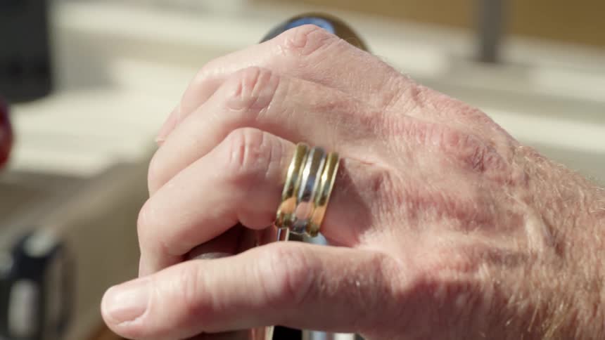 A man moves a lever before resting a hand on the metallic steering wheel of a boat