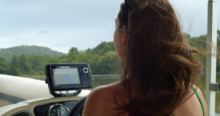 A woman drives a boat on a lake with a gps monitor in front of her
