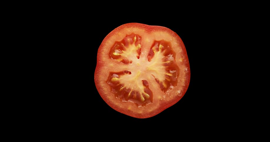 Knife slices off top of tomato against black background