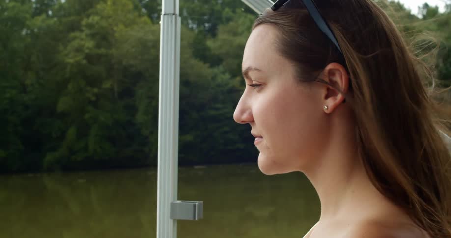 Wind rustles a young womans hair as she drives a boat down a murky brown river during the day