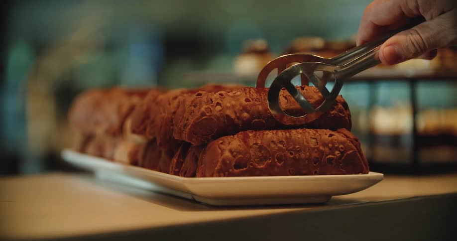 A person removing a pastry from a plate with tongs in a bakery
