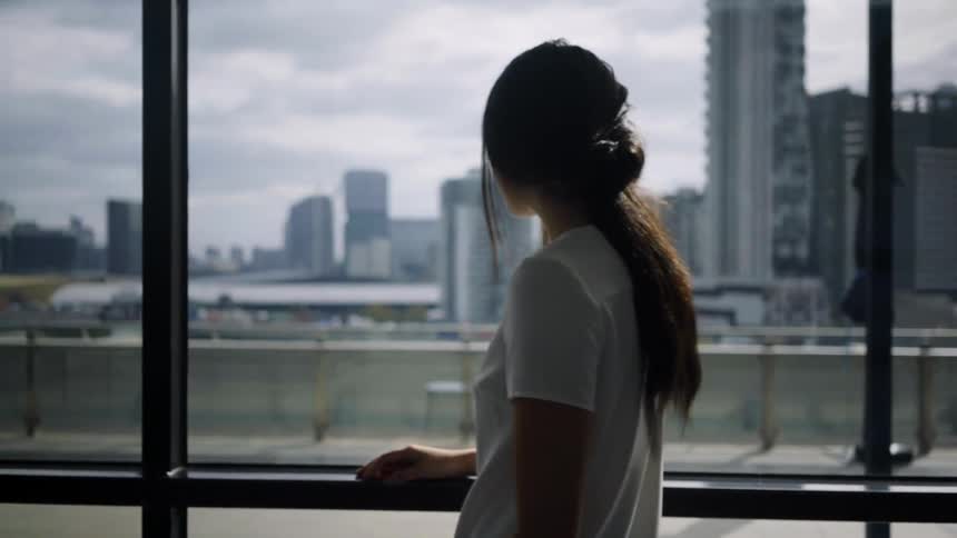 A woman is standing inside a building and looking out a window