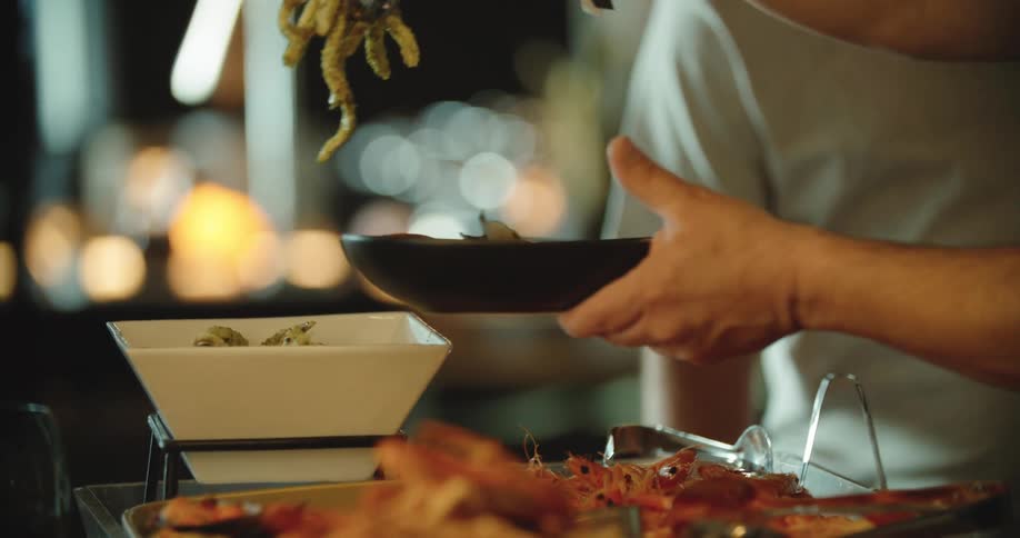 A man uses a pair of metal tongs to retrieve noodles from a bowl and place them on his plate