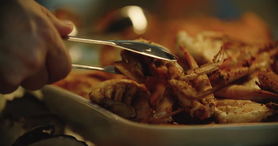 A close view of a man grabbing a cooked crab from a dish with a pair of tongs