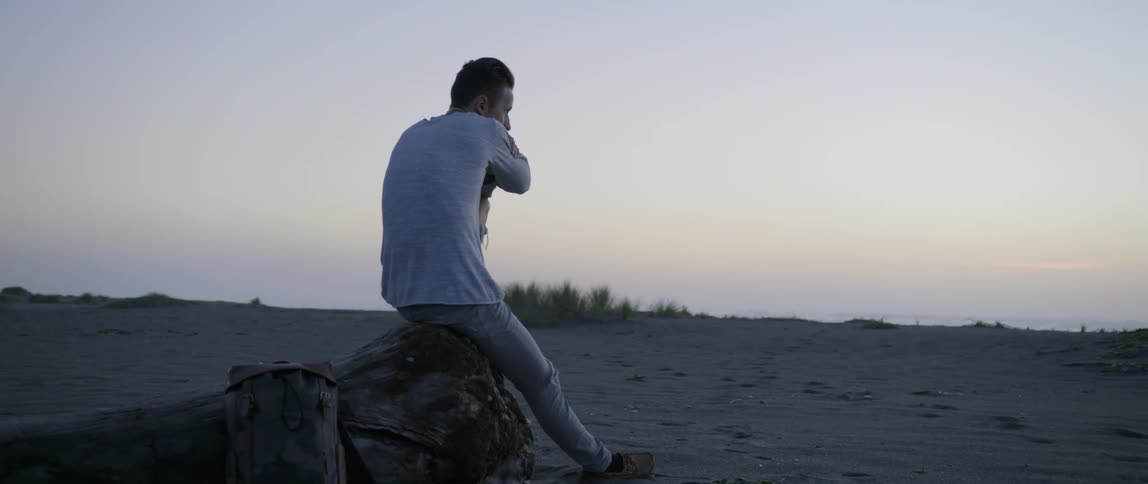 A man sits on a rock on the beach at sunset