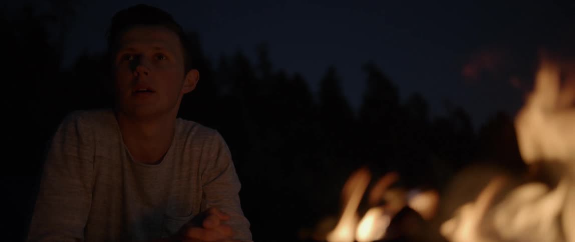 A young man sitting by a campfire