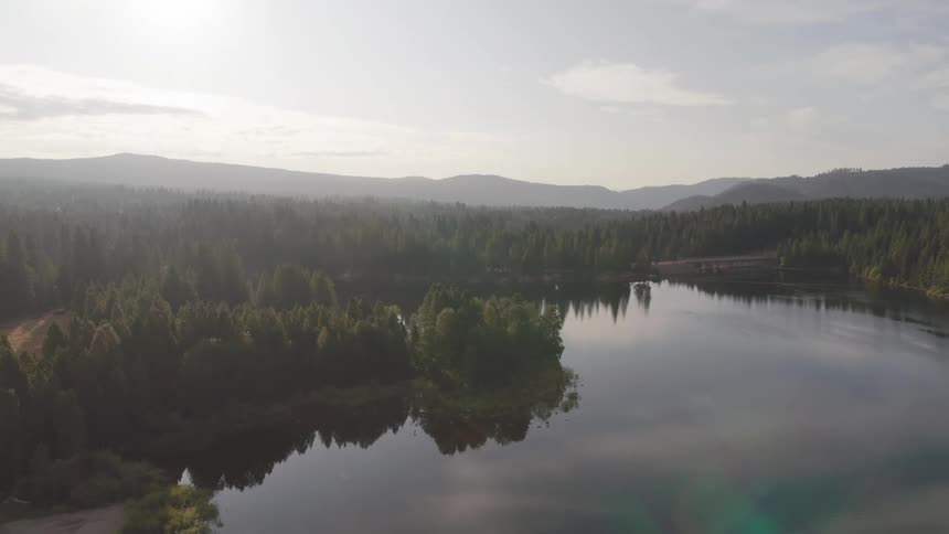 River reflects conifer forest occupying river bend shoreline as mist covers surrounding mountains