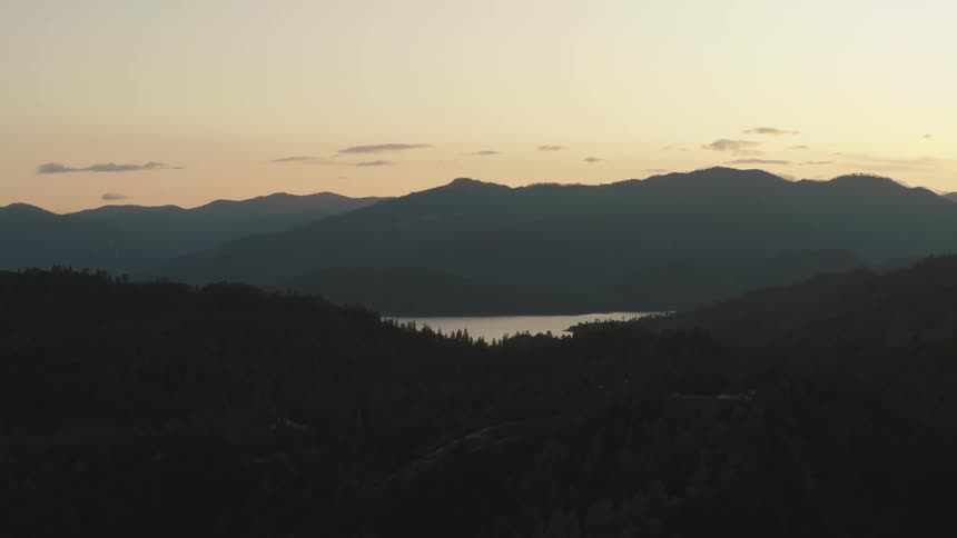 Mountains covered in forest surrounding a lake at sunset