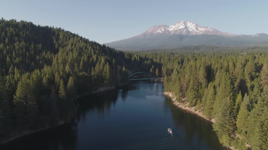 An aerial view of a lake within a forest with a large snow capped mountain in the distance