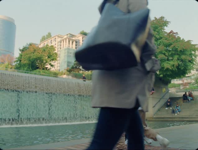 A man break dances on a dance mat in front of a fountain in a park as a woman watches him from the side before the two switch places