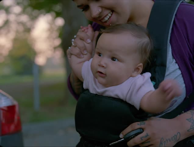 An infant sits in a carrier strapped to her mother while happily wiggling