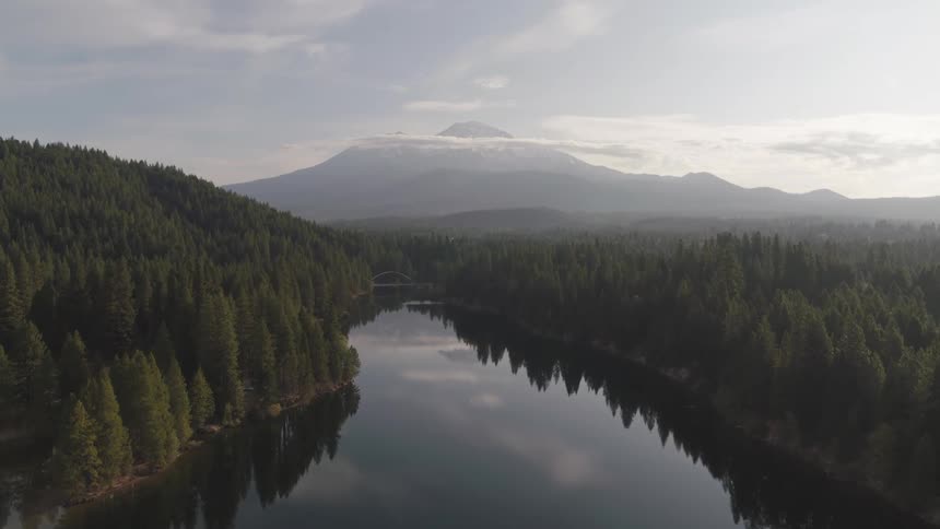 A lake surrounded by trees with a mountain range the sky and clouds in the background