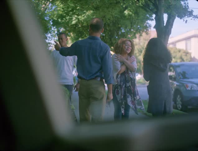 A man and woman come out of their house and greet another couple
