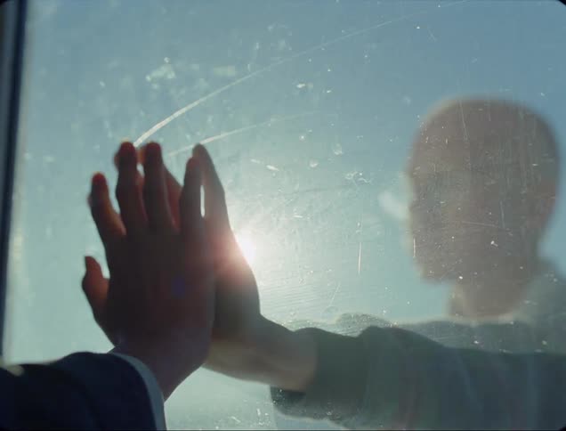 Person reaches up to match hand placement on person on other side of glass