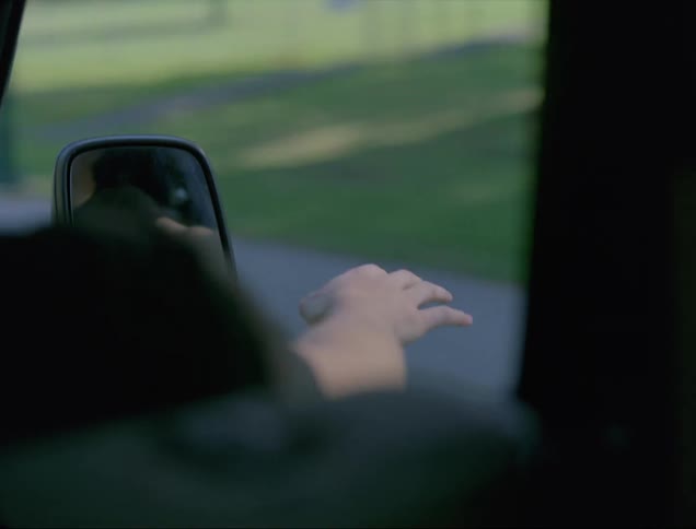 The passenger of a pickup truck rides with his arm sticking out the open window as it drives through a town