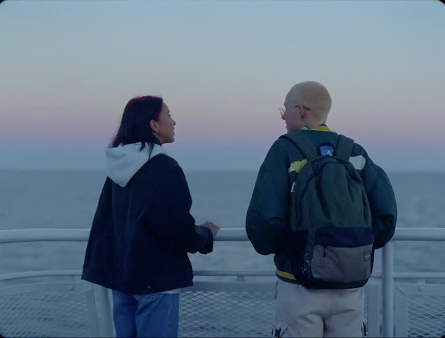 A man and a woman standing by a handrail with the ocean and the sky in the background