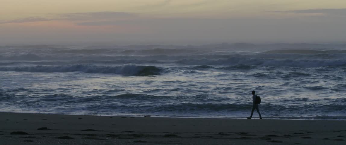 A man is walking along the ocean at sunset