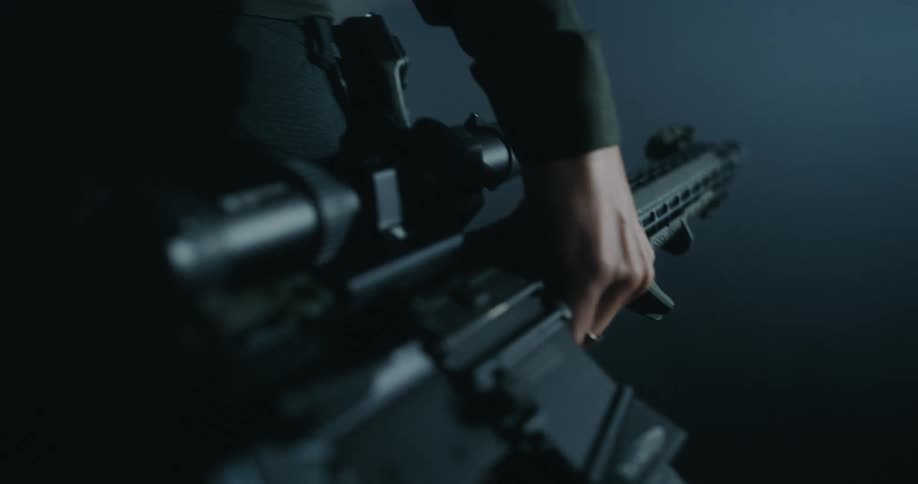 A man carries a large rifle as he walks in the darkness