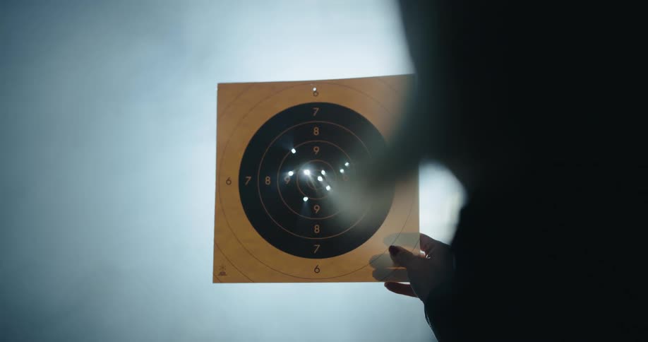 A person looks at their target paper covered in bullet holes
