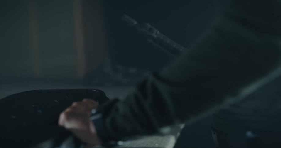 A man places a briefcase and a rifle down on a carpeted table in an empty room