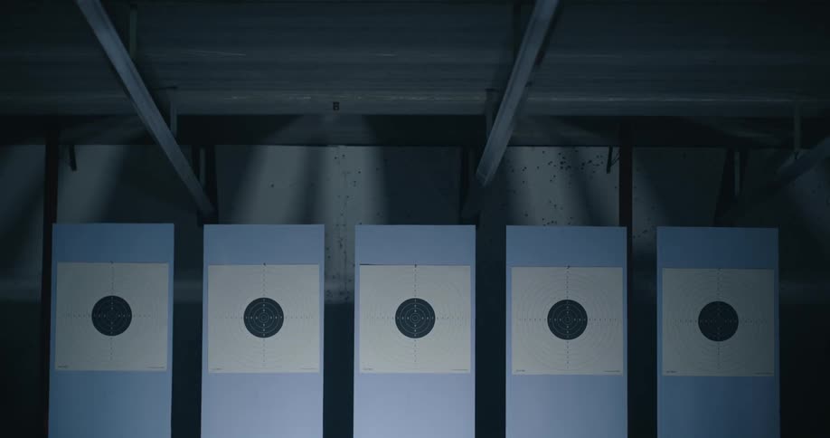 A row of shooting targets turn to face the camera in a dimly lit shooting range