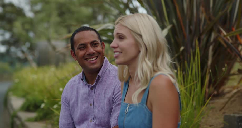 A man and a woman sitting and talking with trees and the sky in the background