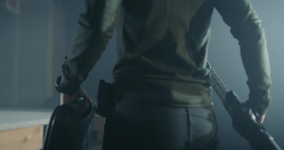 A woman carries a rifle and gun carrying case into a shooting range and places them on a table