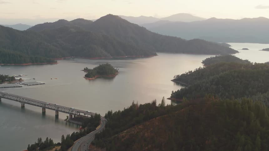 A bridge with vehicles over a river with a mountain range and the sky in the background