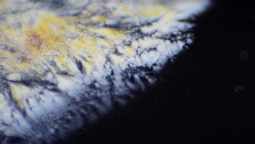 Colorful white and yellow crystals form expanding over a black surface
