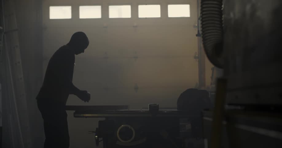 A man lifts up a plank of wood and places it on a table